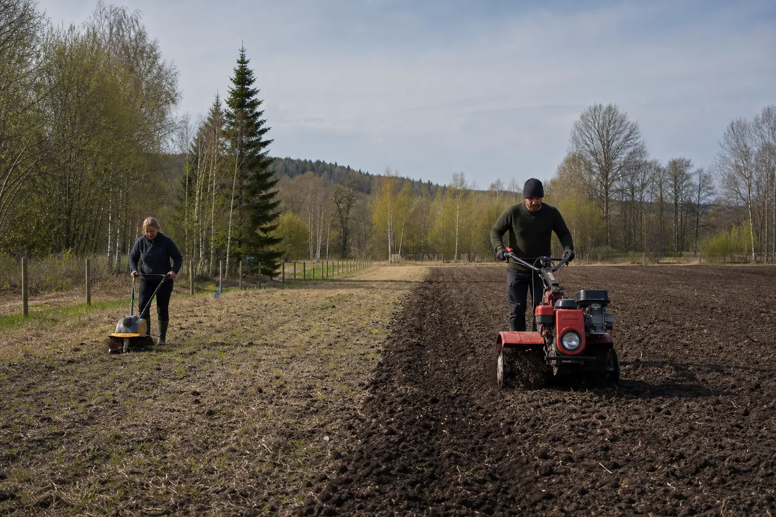 Liten kultivator och större varumärkesfri jordfräs vid ett land.