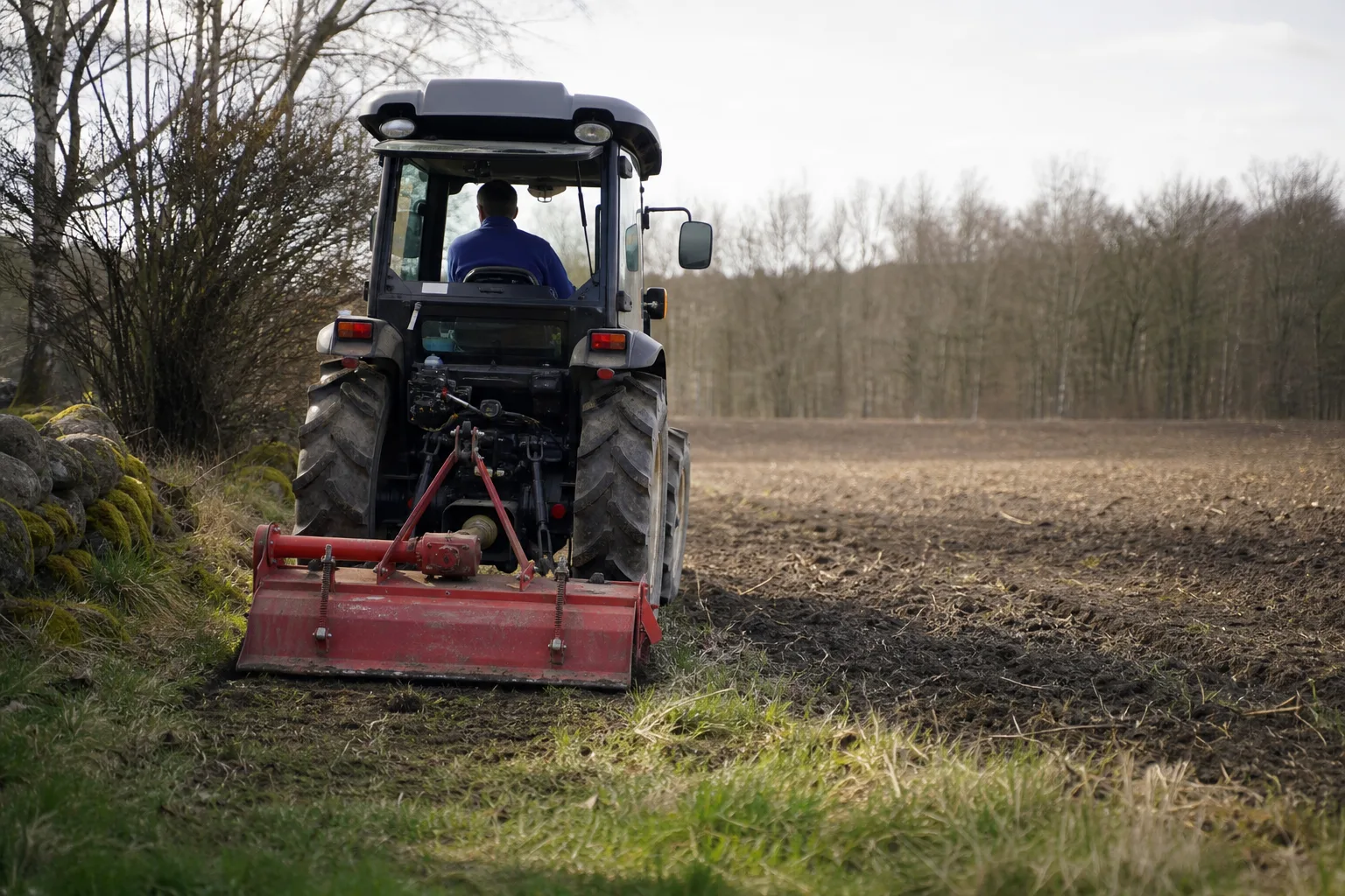 Kompakttraktor bakifrån med varumärkesfri fräs vid åkerkanten.